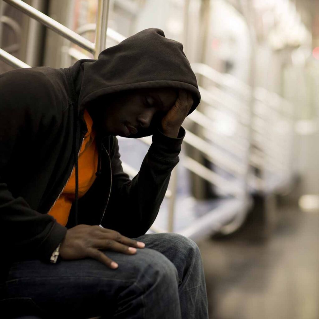 Young man in hoodie sitting on steps with hand on head