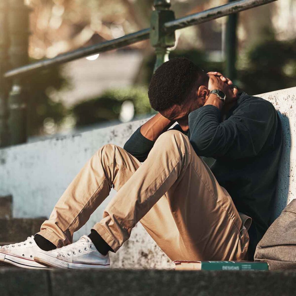 Young man sitting outside holding his head